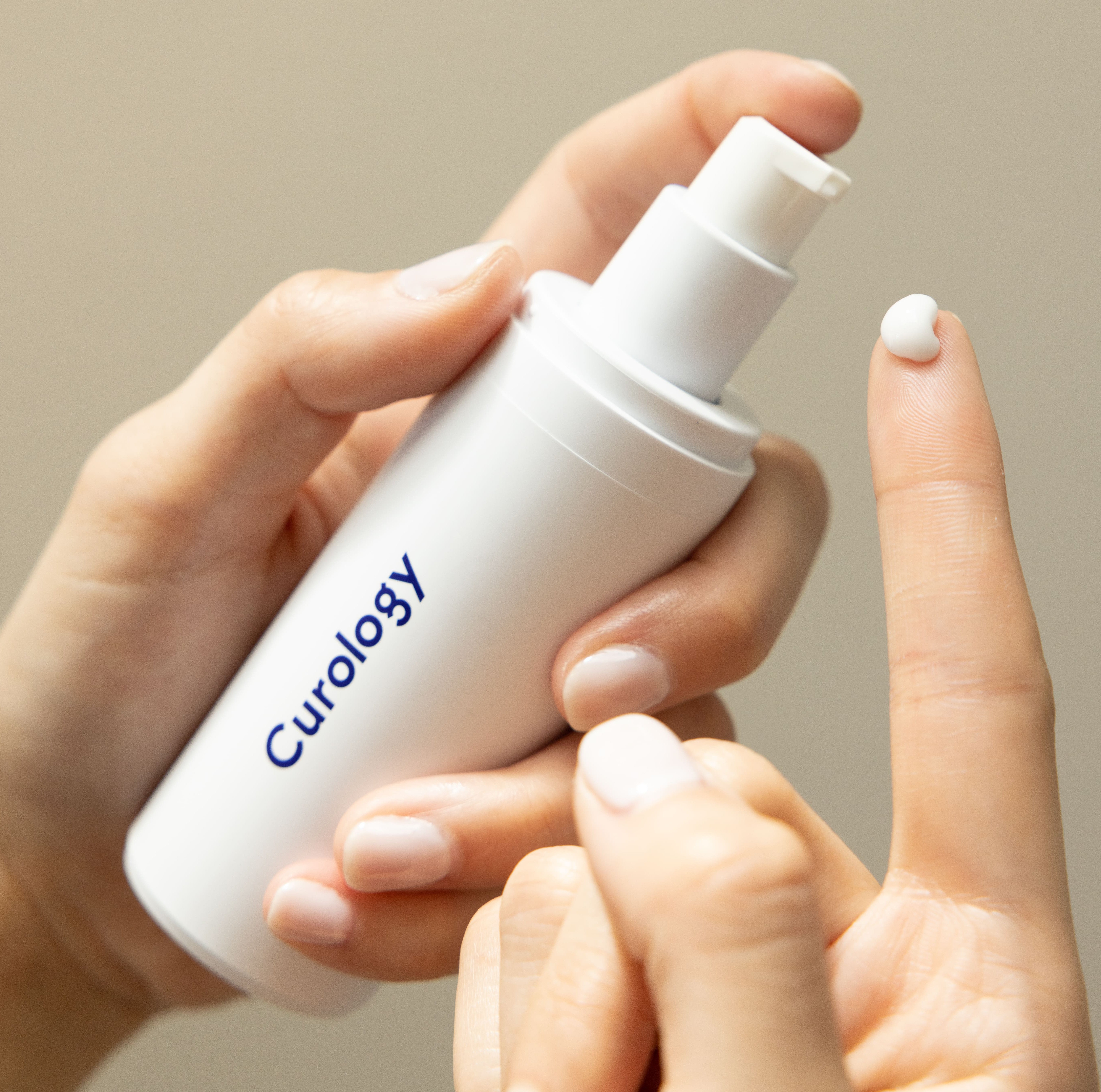 Two hands, the left hand holding a white Curology Custom Formula Rx bottle, the right hand holding up a finger with a pea-size amount of the product.